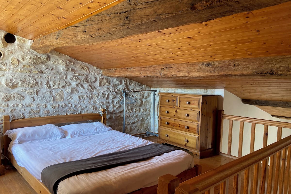 A bedroom with a wooden bed, a stone wall, and a wooden dresser.