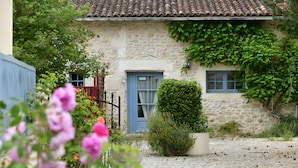 A stone building with a tiled roof, a small garden with gravel, and a blue door. - Domaine Les Granges (Ternant)
