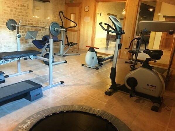 Un gimnasio con varios equipos de ejercicio, incluyendo una prensa de banca, máquinas de pesas y una elíptica.