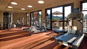A gym with cardio machines, weight training equipment, and large windows offering a mountain view. - Spacious + Modern Suite | Minutes from Whistler (Whistler)