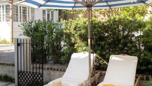 Two sun loungers with a striped umbrella, a wooden deck, and a house in the background. - Green Cottage – Private Casa Zoë Downtown Stay (Charleston)