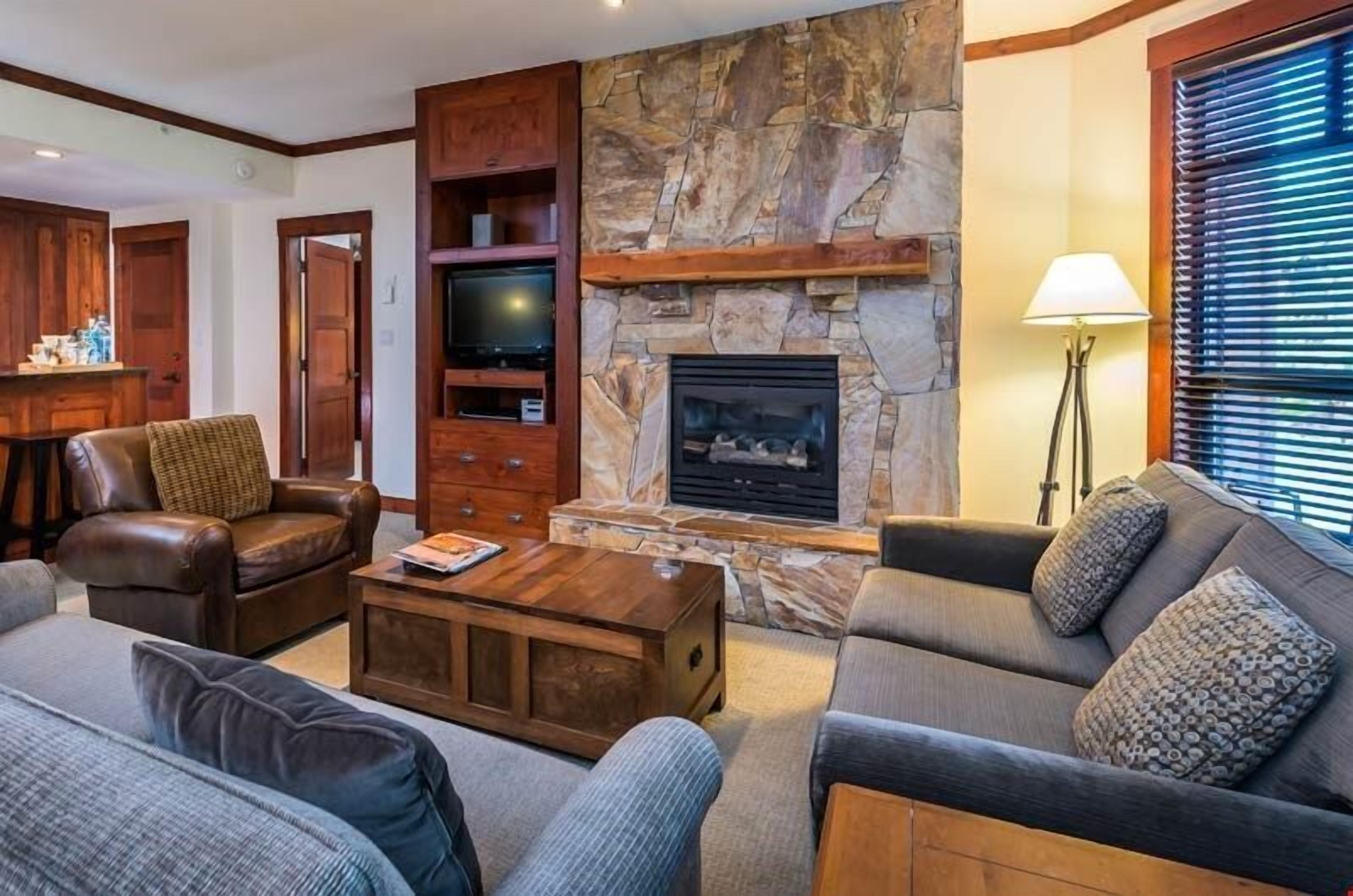 Una sala de estar acogedora con chimenea de piedra, muebles de cuero y una televisión.