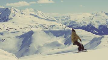 Un snowboardeur sur une pente enneigée d’une montagne, avec des sommets couverts de neige en arrière-plan.