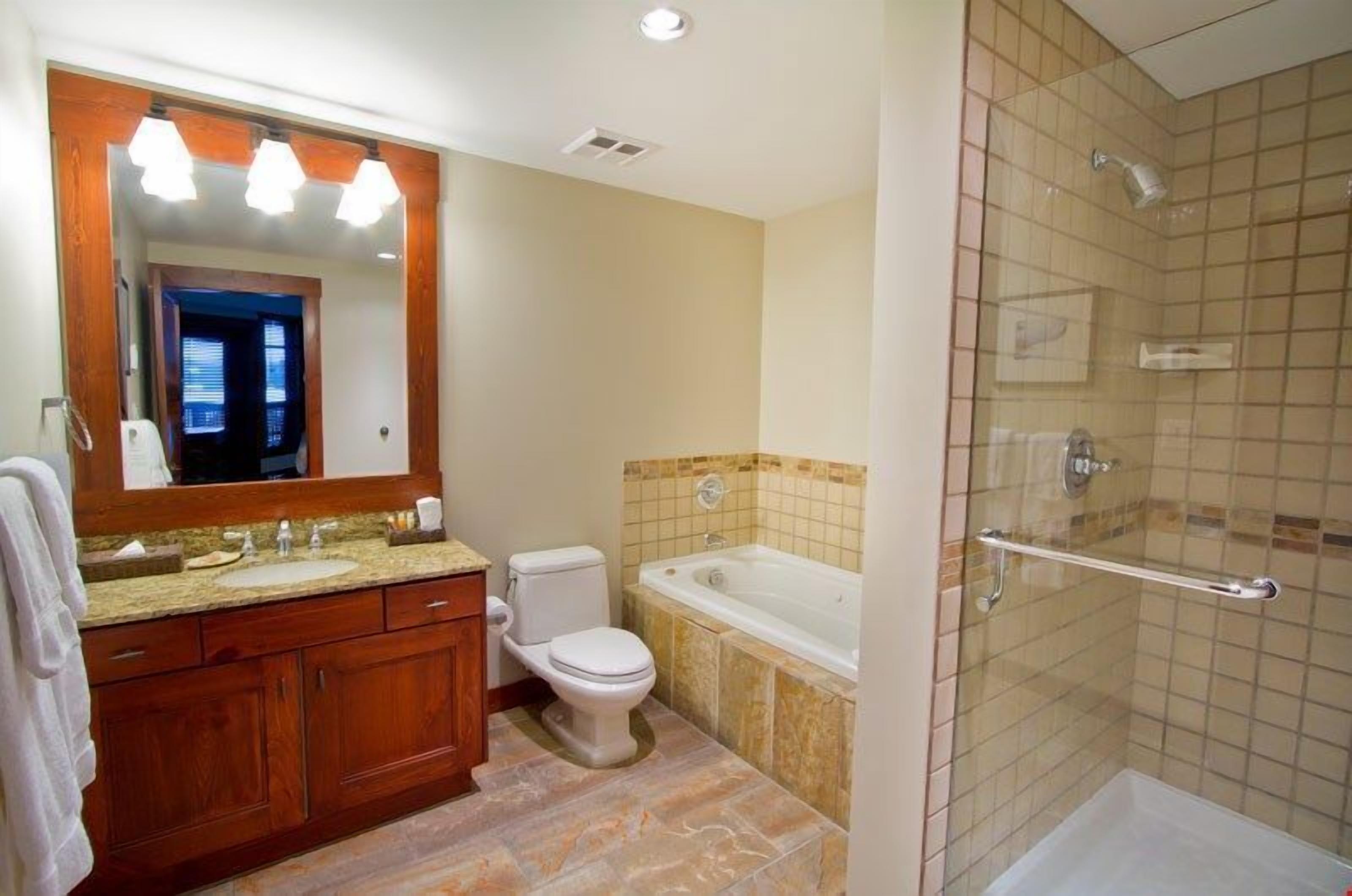 Un baño con tocador de madera, inodoro, bañera y zona de ducha con cerramiento de vidrio.
