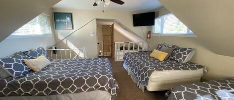 Une chambre avec deux lits, un ventilateur de plafond, une télévision et un escalier menant à un niveau supérieur.