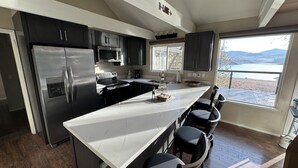 A modern kitchen with a central island, stainless steel appliances, and a view of a lake. - Top Lakefront Oasis - Kayaks, Paddle Bd, - Shasta Lakeshore Retreat #2 (Lakehead)