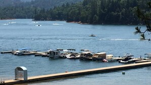 A marina with boats docked, a dock extending into the water, and a forested hillside in the background. - Top Lakefront Oasis - Kayaks, Paddle Bd, - Shasta Lakeshore Retreat #2 (Lakehead)
