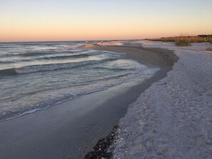 Une plage avec des vagues, du sable et une végétation clairsemée.