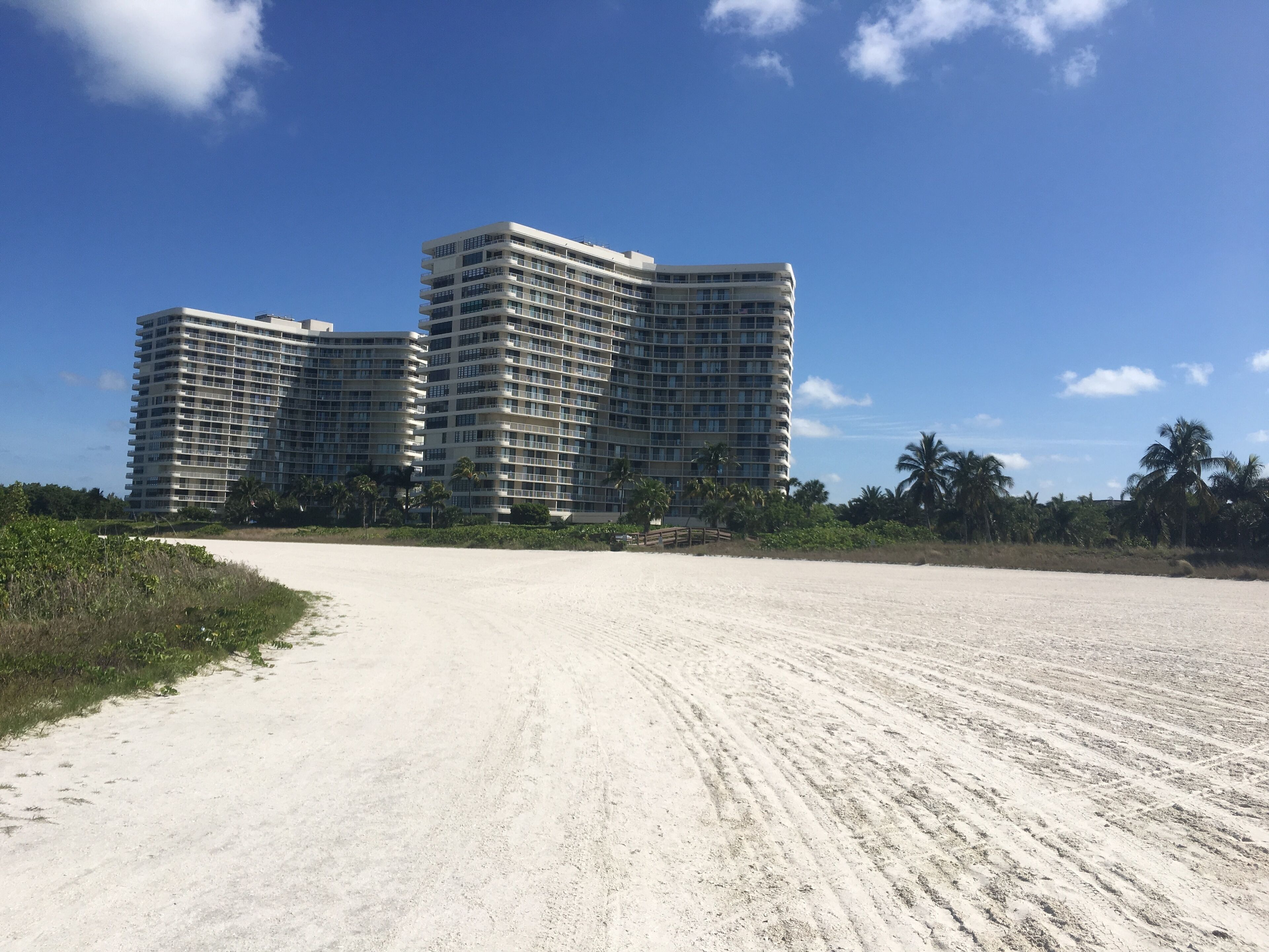 A beachfront hotel with multiple high-rise buildings, a sandy beach, and palm trees.