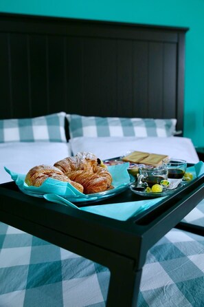 A bed with a checkered bedspread, a tray with croissants, a glass of water, and a cup of coffee on a bedside table. - Affittacamere Andolfi 24 (Pompei)
