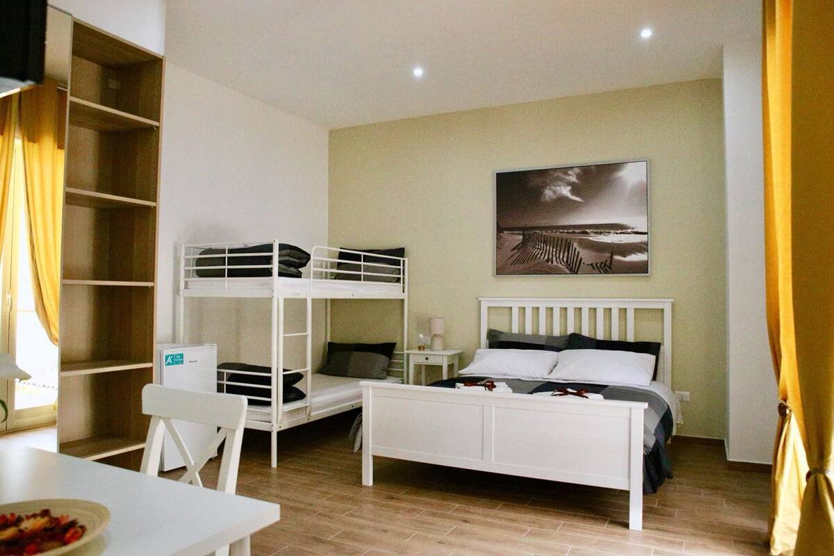 Une chambre de type dortoir, avec des lits superposés, un bureau, une chaise, une table de chevet et un tableau accroché au mur.