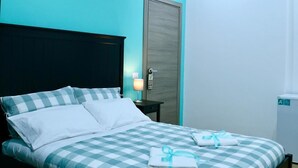 A modern bedroom with a checkered bedspread, a dark headboard, an air conditioning unit, a nightstand with a lamp, and a door with a handle. - Affittacamere Andolfi 24 (Pompei)