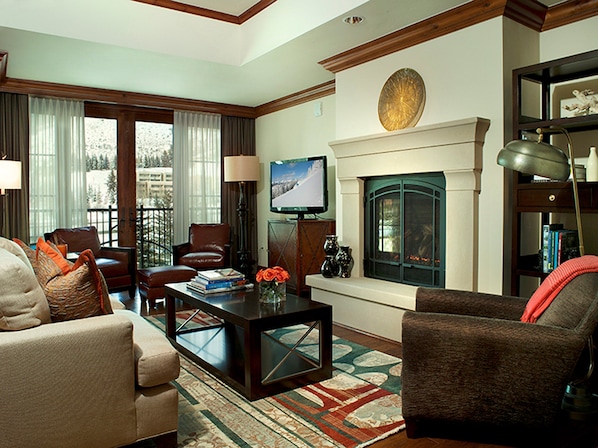A living room with a fireplace, a television, and a bookshelf. - Valley View Condo | Pool & Whirlpool on site! (Vail)