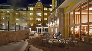 En hotelgård med udendørs siddepladser og bålsted, omgivet af høje bygninger med altaner og store vinduer.