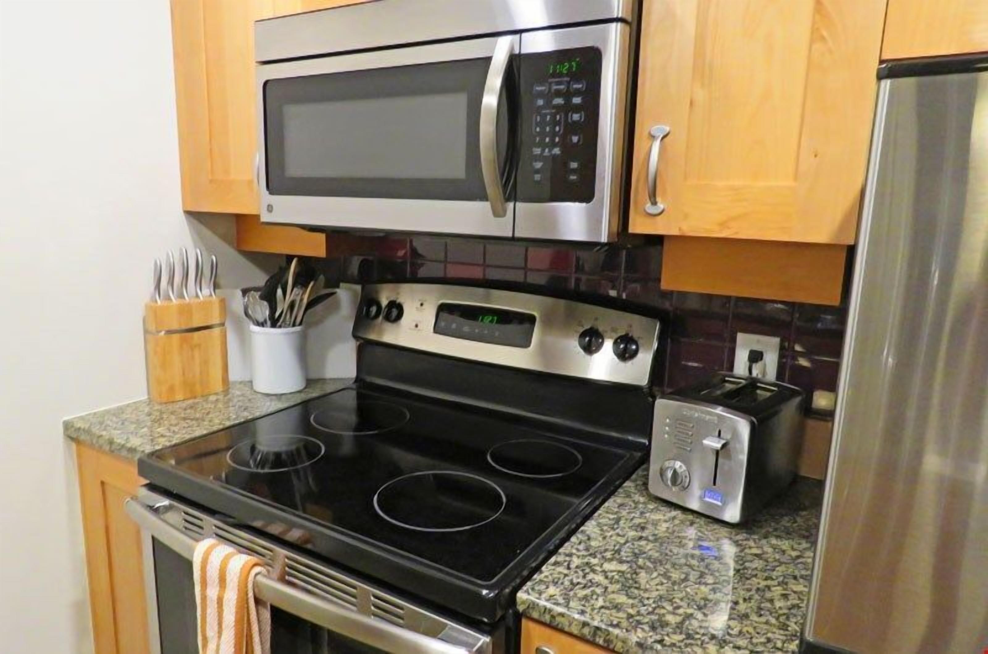 A kitchen with a stainless steel microwave, a built-in oven, a toaster, and wooden cabinets.