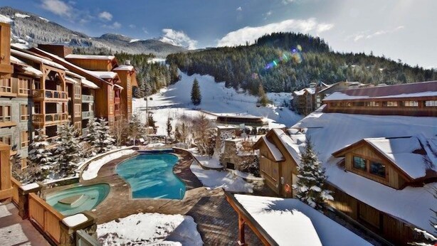 Un complejo turístico con varias cabañas de madera, una piscina y montañas nevadas al fondo.