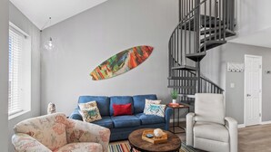 Un salon moderne avec un canapé bleu, un fauteuil blanc, une table basse ronde et un tableau abstrait aux couleurs vives.