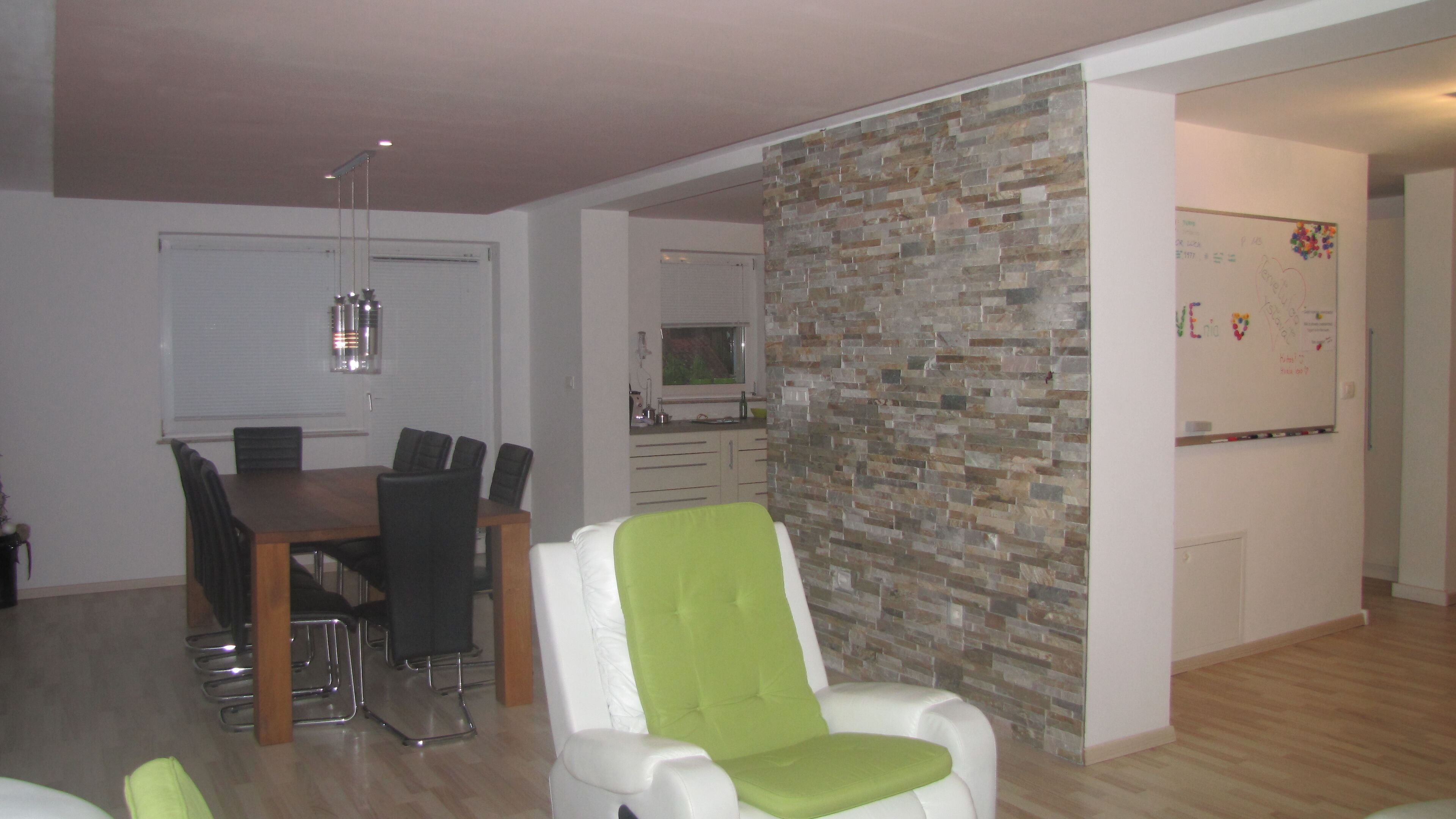 A modern dining area with a wooden table and chairs, a stone accent wall, and a whiteboard with writing.