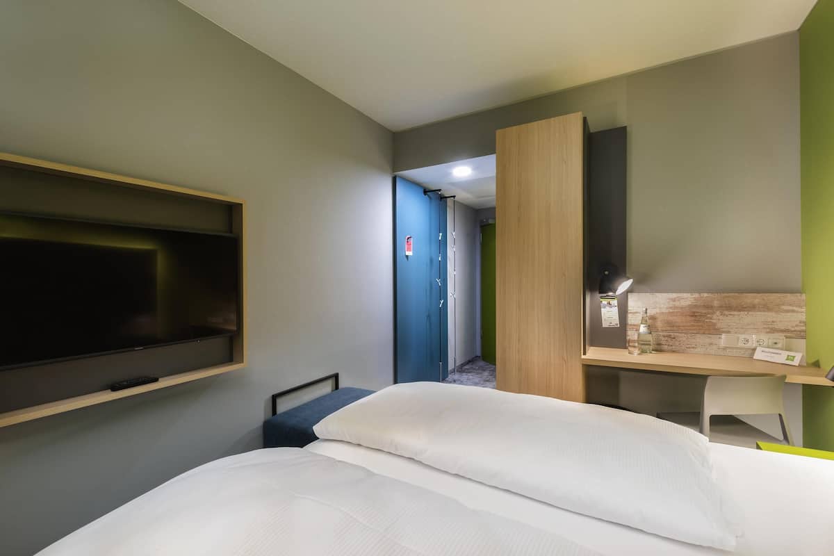 Una habitación de hotel con una cama, un escritorio, un televisor y una puerta que da a otra habitación.