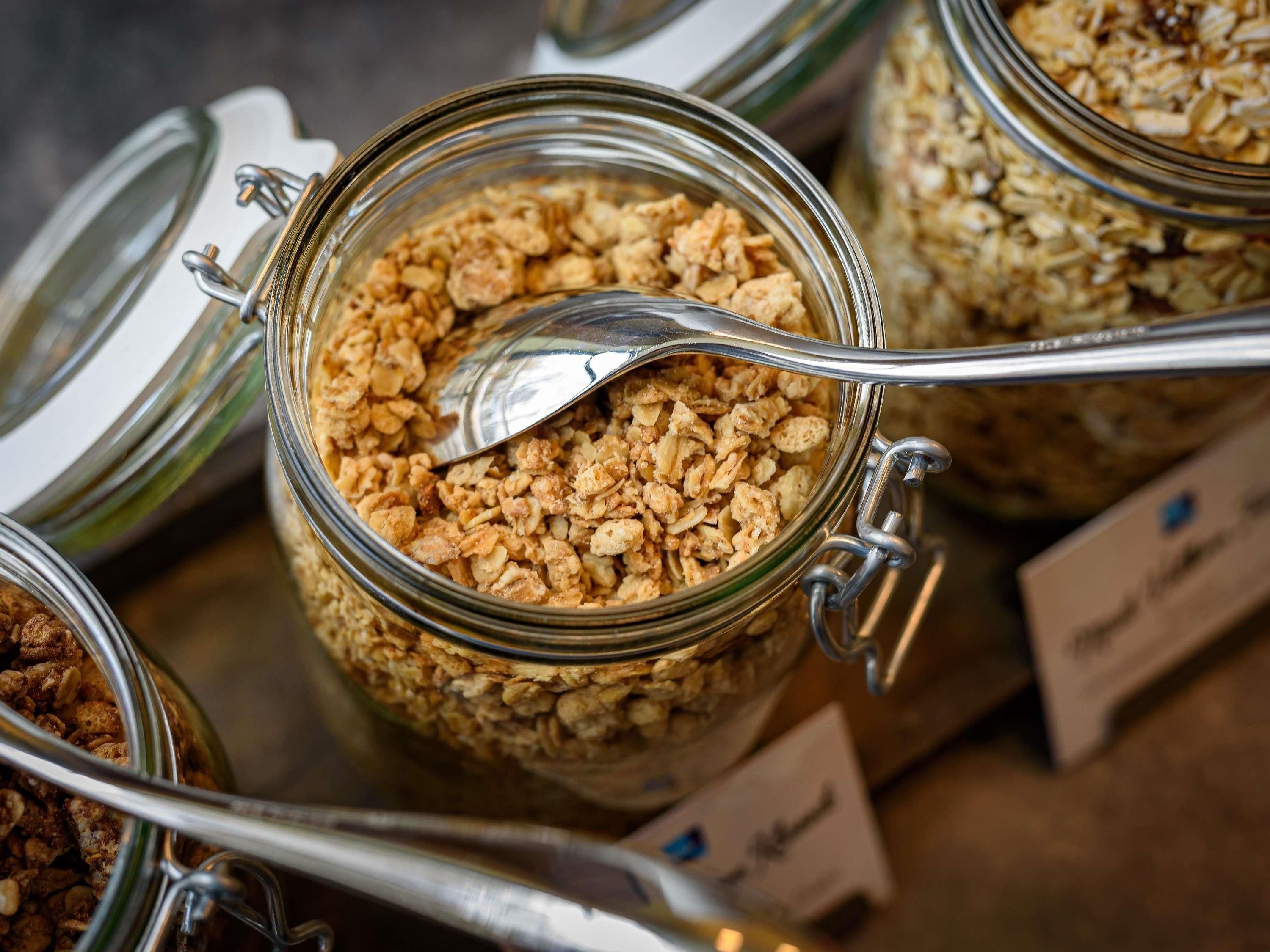 A close-up of a glass jar with granola, a spoon inside, and a metal clasp lid.