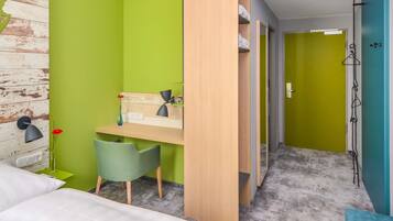 Une chambre à coucher avec un lit, un bureau et une chaise, une armoire et une salle de bain visible à travers une porte ouverte.