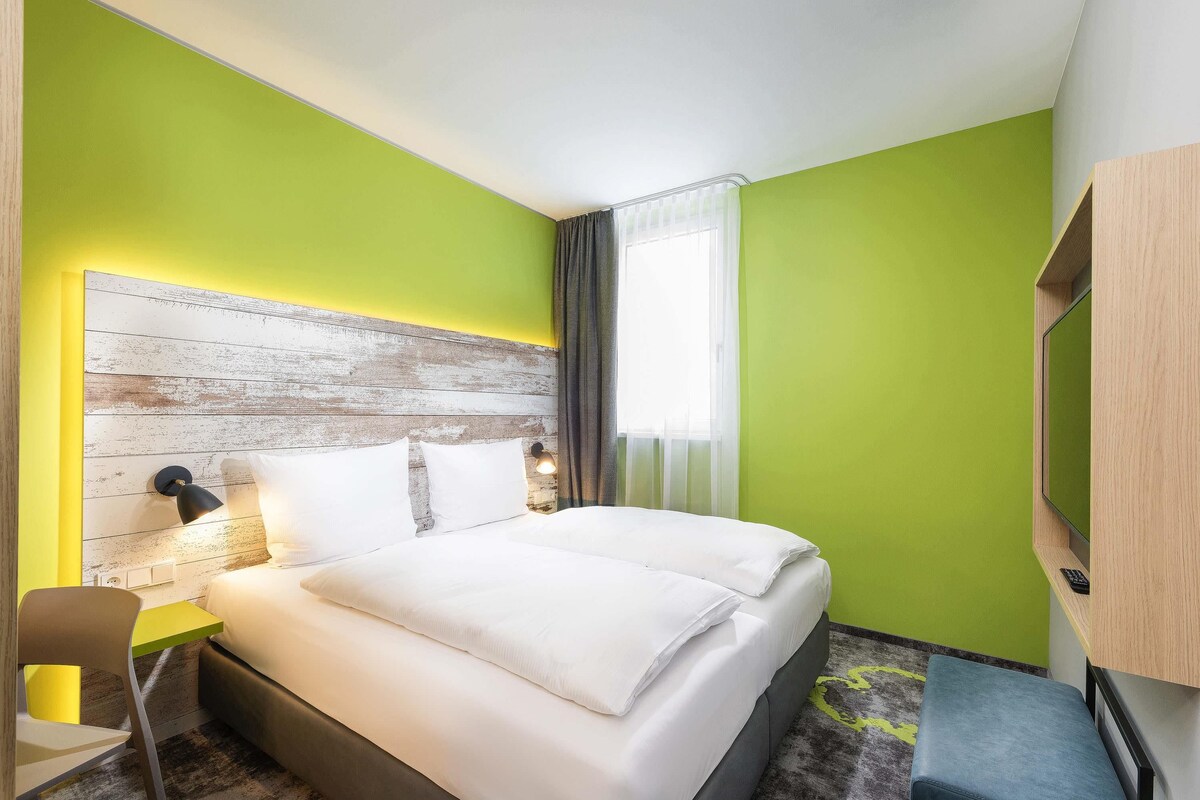 Una habitación de hotel con una cama, una silla, un escritorio y un televisor.