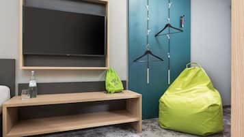 Una habitación con un banco de madera, una bolsa verde, un perchero colgado y un televisor montado en la pared.
