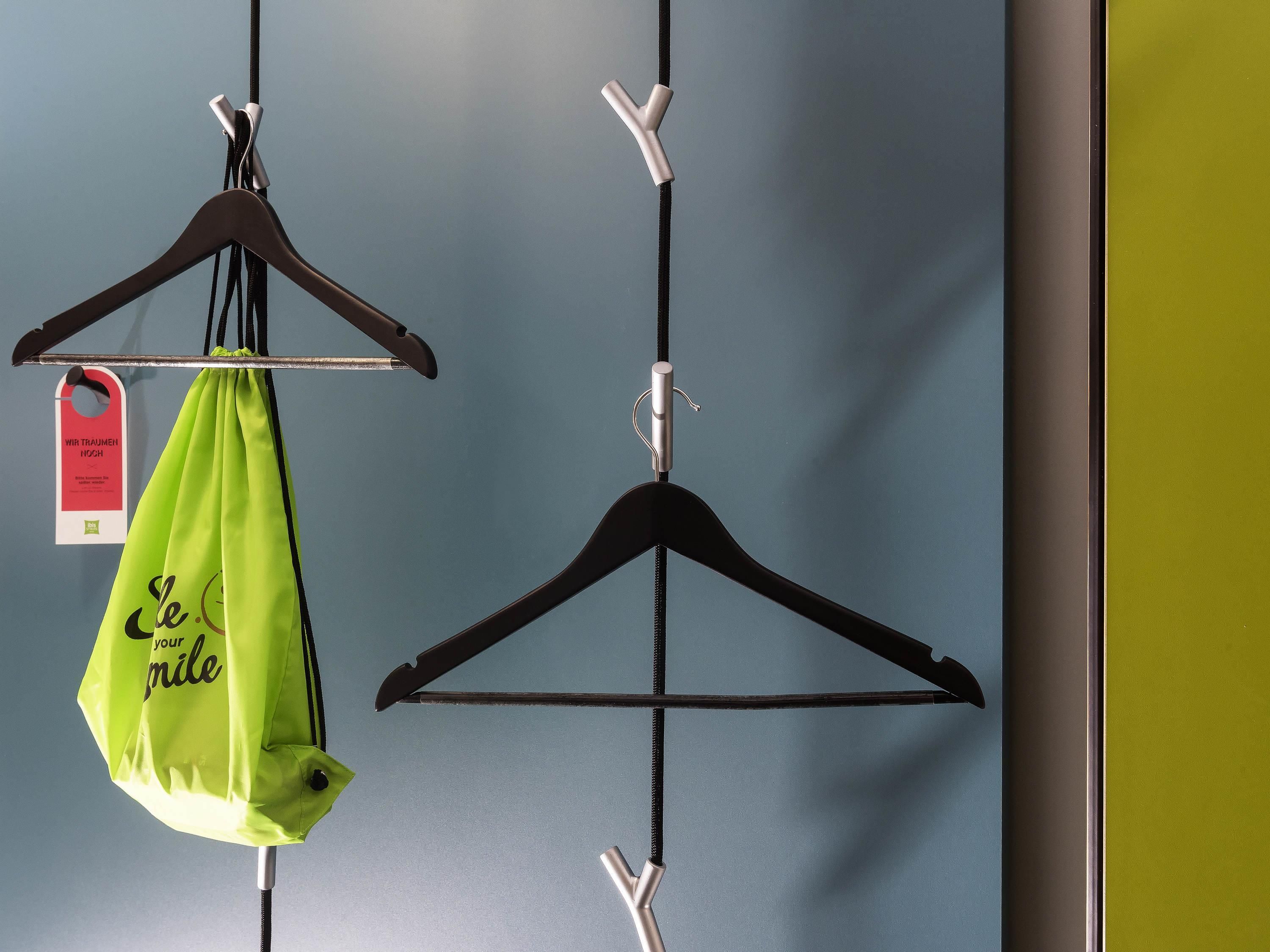 Una pared con dos perchas negras, una con una bolsa verde colgada.