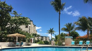 Una piscina con sillones de descanso y palmeras, rodeada de edificios.
