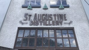 Exterior de St. Augustine Distillery, con fachada texturizada, dos ventanas con luces verdes colgantes y un escaparate grande.
