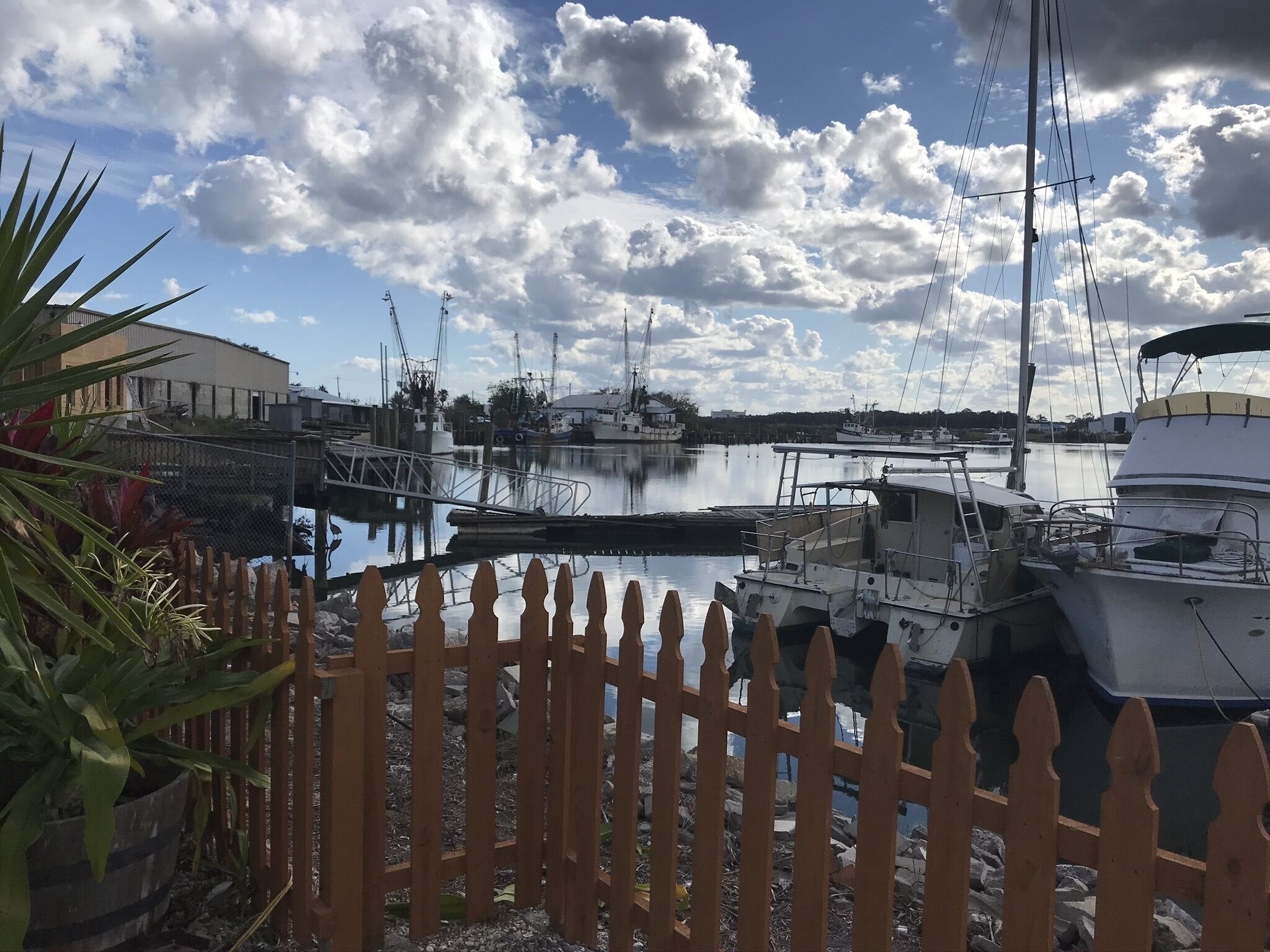 A marina with boats docked, a wooden fence, and a clear sky with clouds.