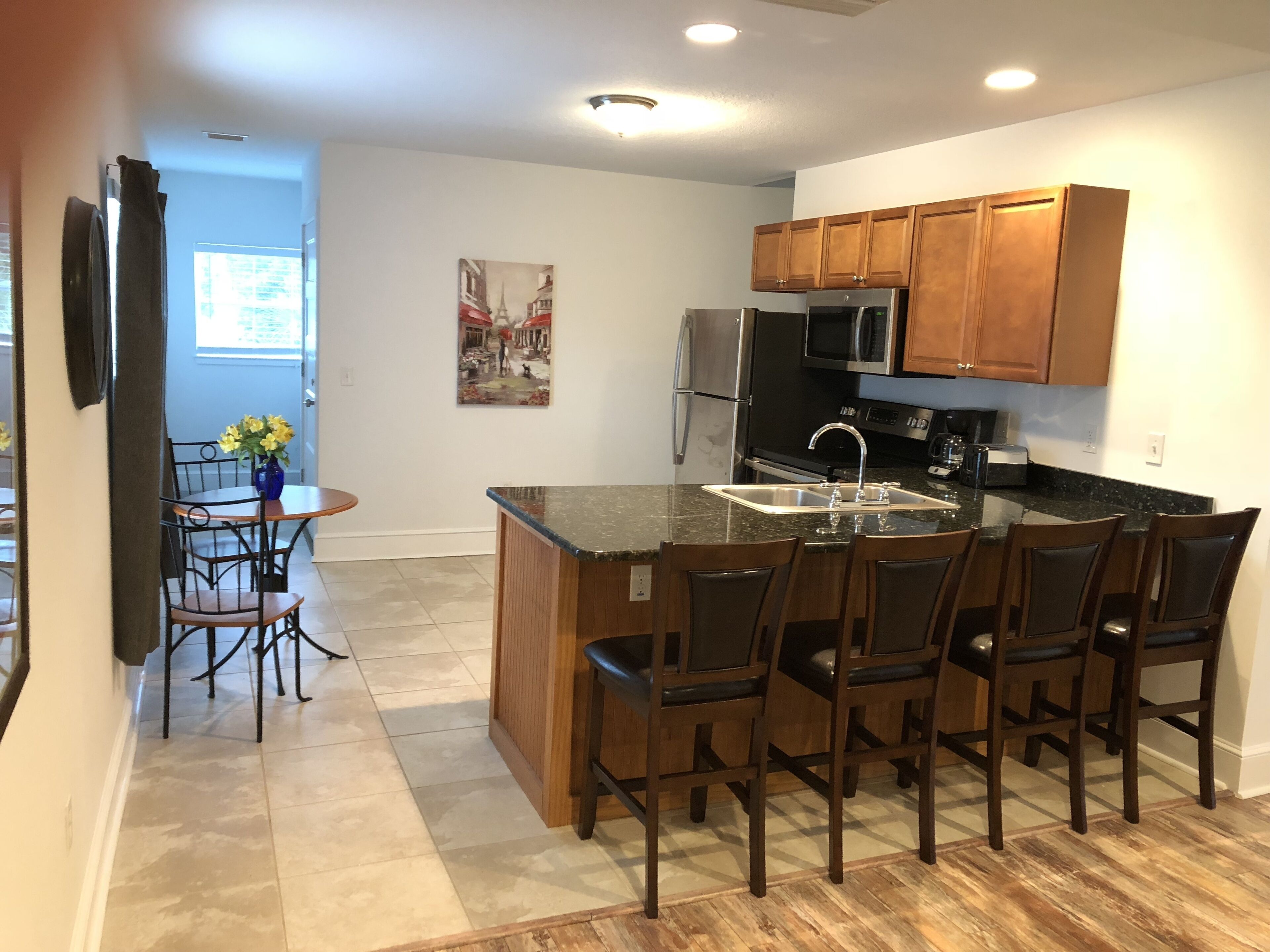 A modern kitchen with wooden cabinets, a stainless steel refrigerator, a microwave, and a sink. There is a dining area with a table and chairs.