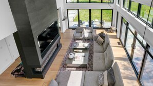 A modern living room with a fireplace, large windows, and a comfortable seating area. - Modern 6Bed-6Bath New in 2023! (Edgartown)