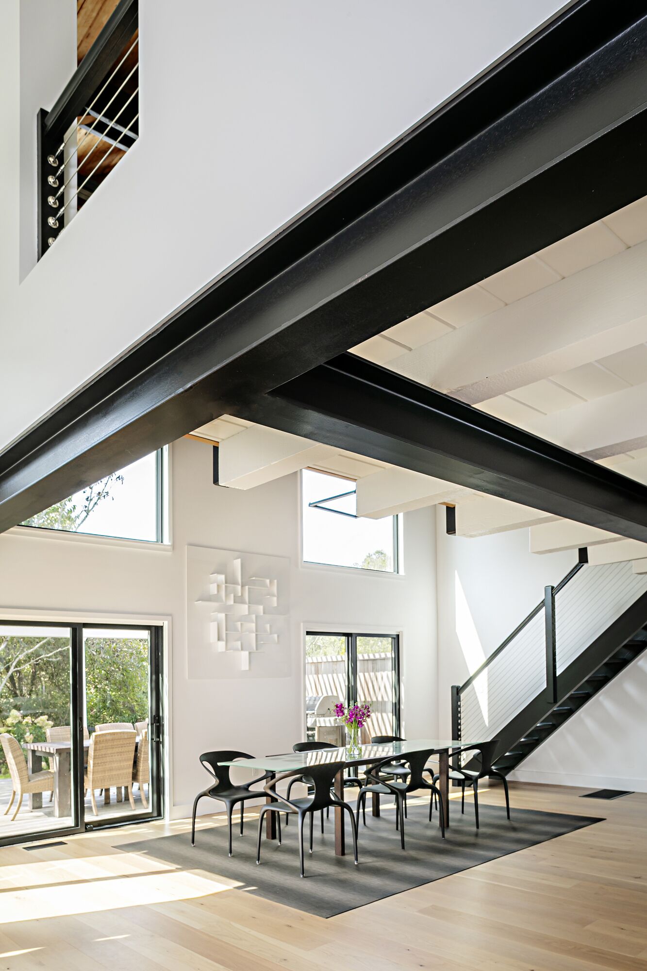 Un intérieur moderne comprenant un coin repas, un escalier et de grandes fenêtres.