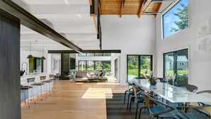 A spacious, modern kitchen with a long island and bar seating, large windows, and a view of the outdoors. - Modern 6Bed-6Bath New in 2023! (Edgartown)