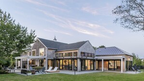 A modern two-story house with a large patio area, large windows, and a covered outdoor seating area. - Modern 6Bed-6Bath New in 2023! (Edgartown)