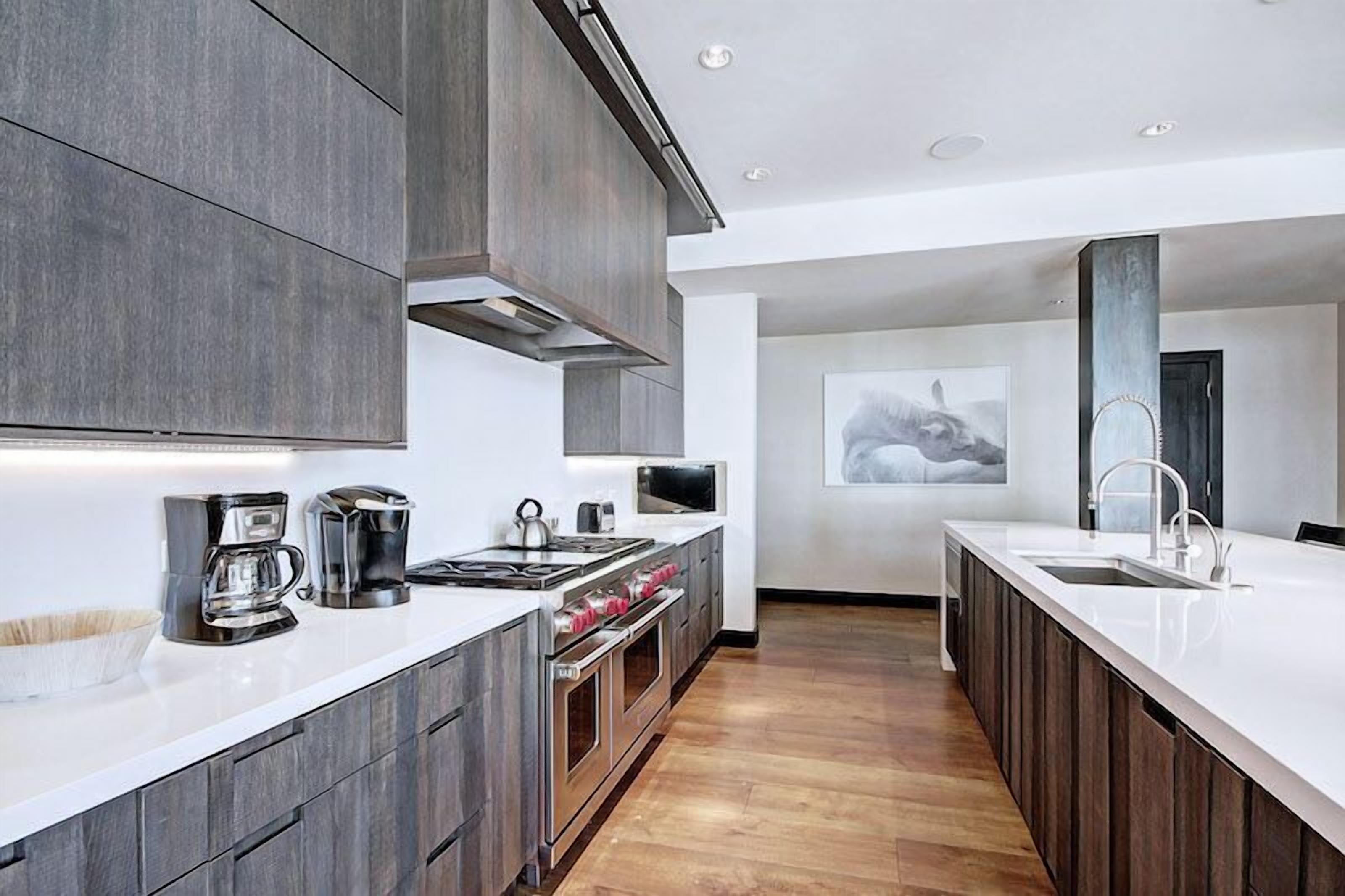 Een moderne keuken met donkerhouten kastjes, een wit aanrecht, roestvrijstalen apparatuur en een groot raam.