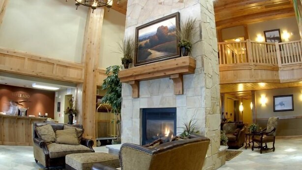A spacious lobby with a stone fireplace, leather sofas, a chandelier, and a balcony overlooking the interior.