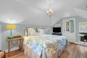 Une chambre à coucher avec un lit, un lustre, une télévision et une fenêtre avec des stores.