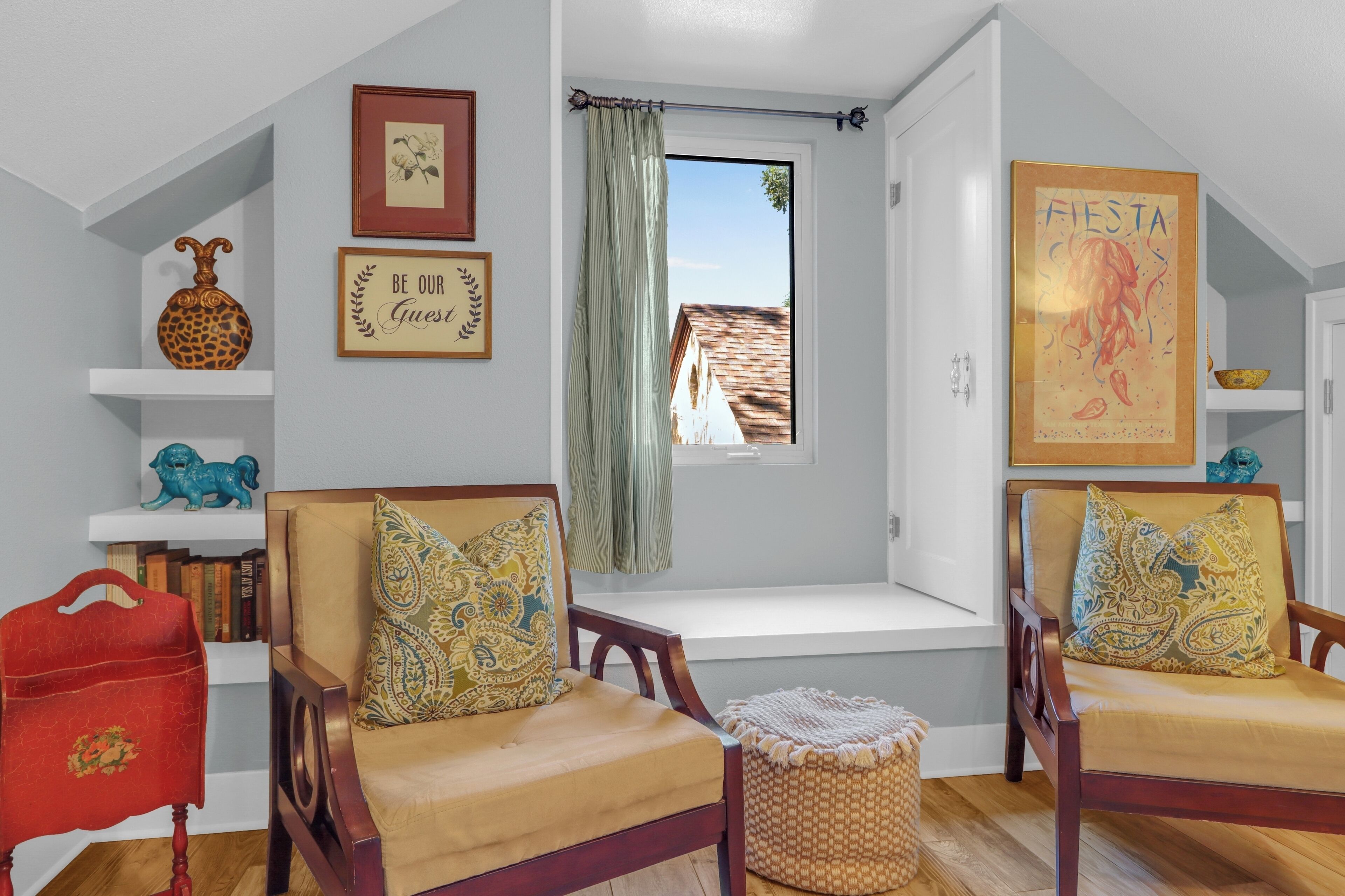 A room with two wooden chairs, a bench, a bookshelf, a red bag, and a window with a view of a building.