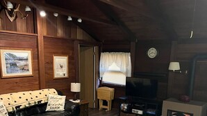 A cozy cabin interior with a black leather sofa, a television, and wooden walls.
