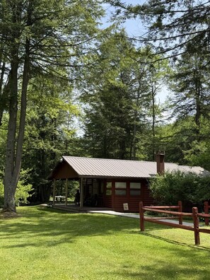 Eine rustikale Holzhütte mit Metalldach, umgeben von hohen Bäumen und einem gepflegten Rasen.