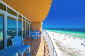 Un balcon avec des chaises et des tables donnant sur une plage parsemée de parasols.