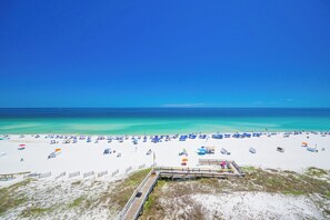 Une plage de sable blanc, une promenade en bois et des parasols.