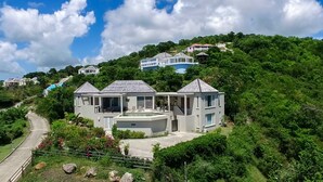 Ein großes, zweistöckiges Haus mit Swimmingpool, umgeben von üppiger Vegetation und Hügeln.