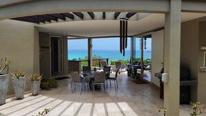 Ein überdachter Außenbereich mit Tisch, Stühlen, einem Grill und Blick aufs Meer.