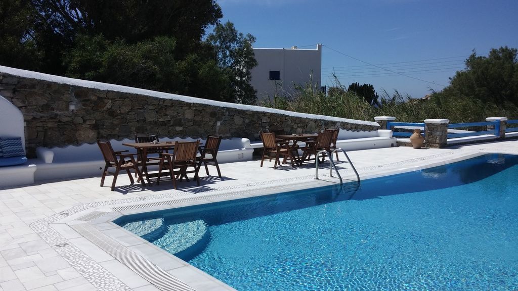 Piscina com muro de pedra e mesa com cadeiras.