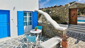 Un edificio blanco con puertas y ventanas azules, un muro de piedra y una piscina al fondo.