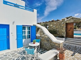 Un edificio blanco con puertas y ventanas azules, un muro de piedra y una piscina al fondo.