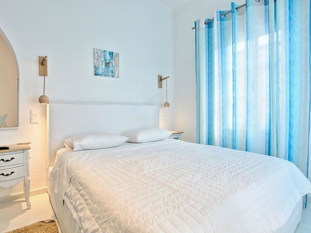 Une chambre à coucher avec un grand lit, des murs blancs et un rideau bleu.